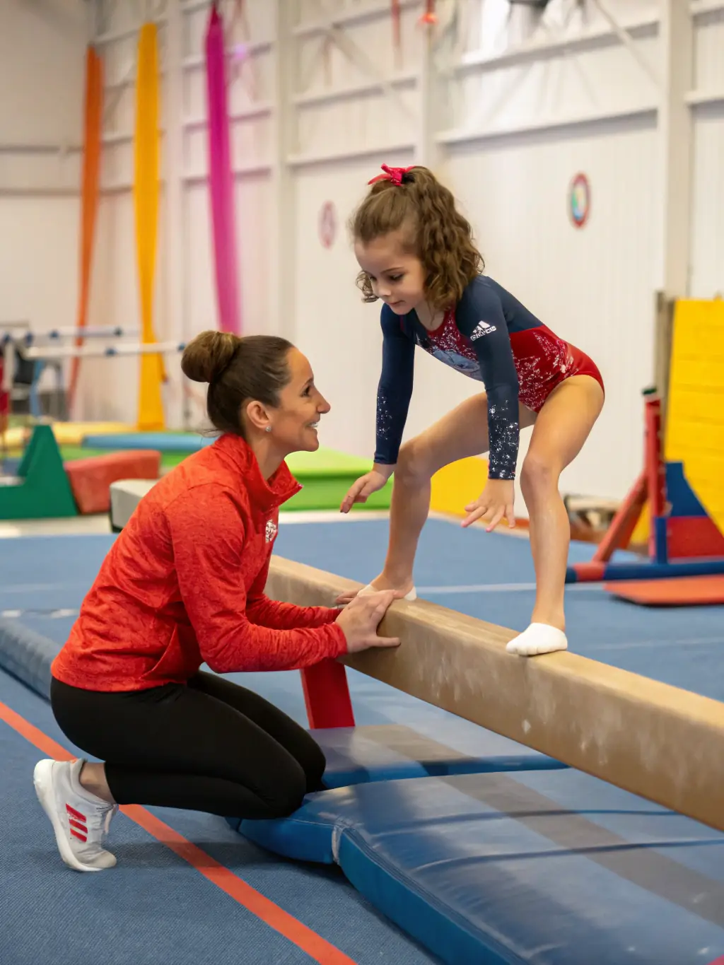 A dynamic shot of an experienced gymnastics coach demonstrating a technique to a young gymnast at Gym Club Houdanais, showcasing the club's dedication to expert instruction.